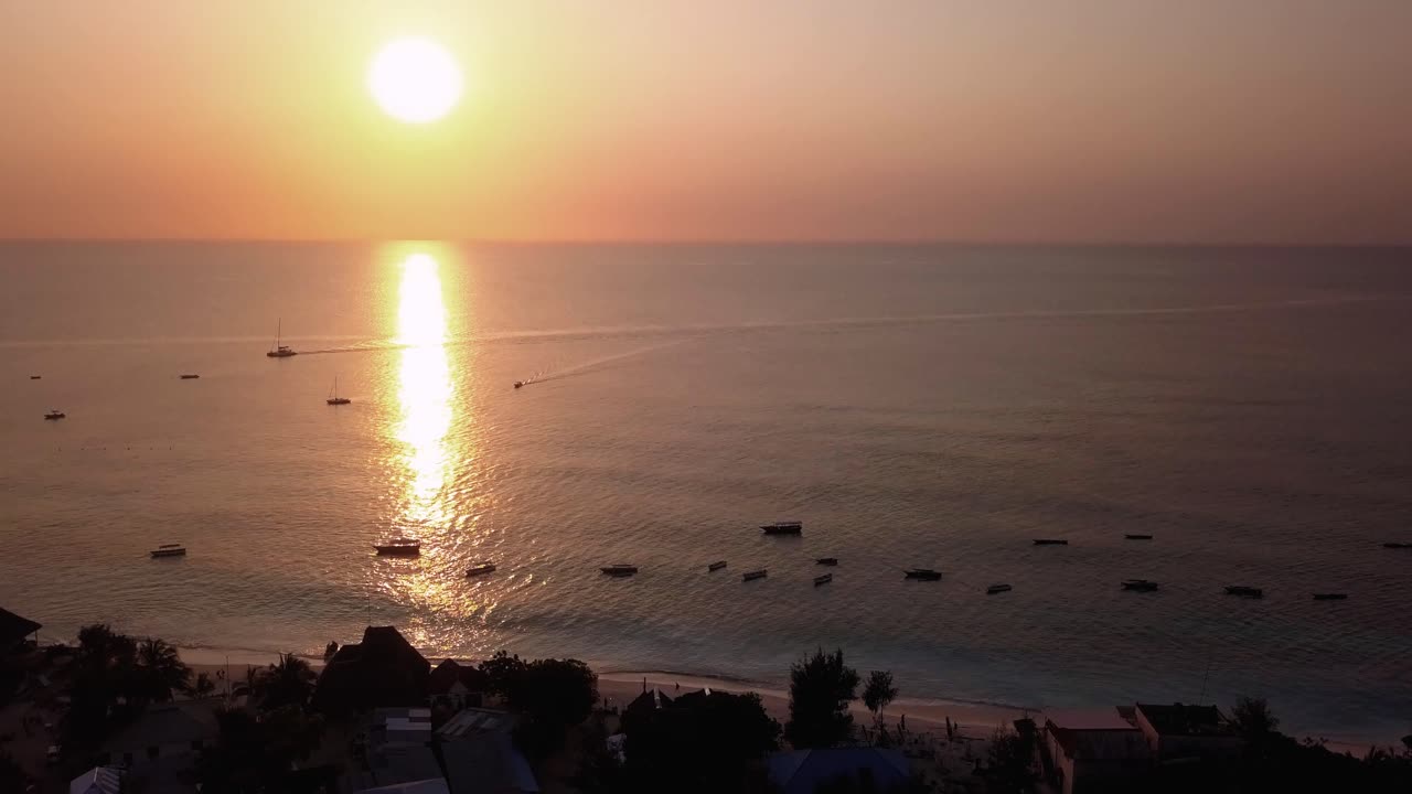 Boats sit Anchored in the Ocean During Sunset, While the Sun Reflects of the Tropical Water Nungwi Beach, Zanzibar, Island in Tanzania Drone Pullback Tilt Up