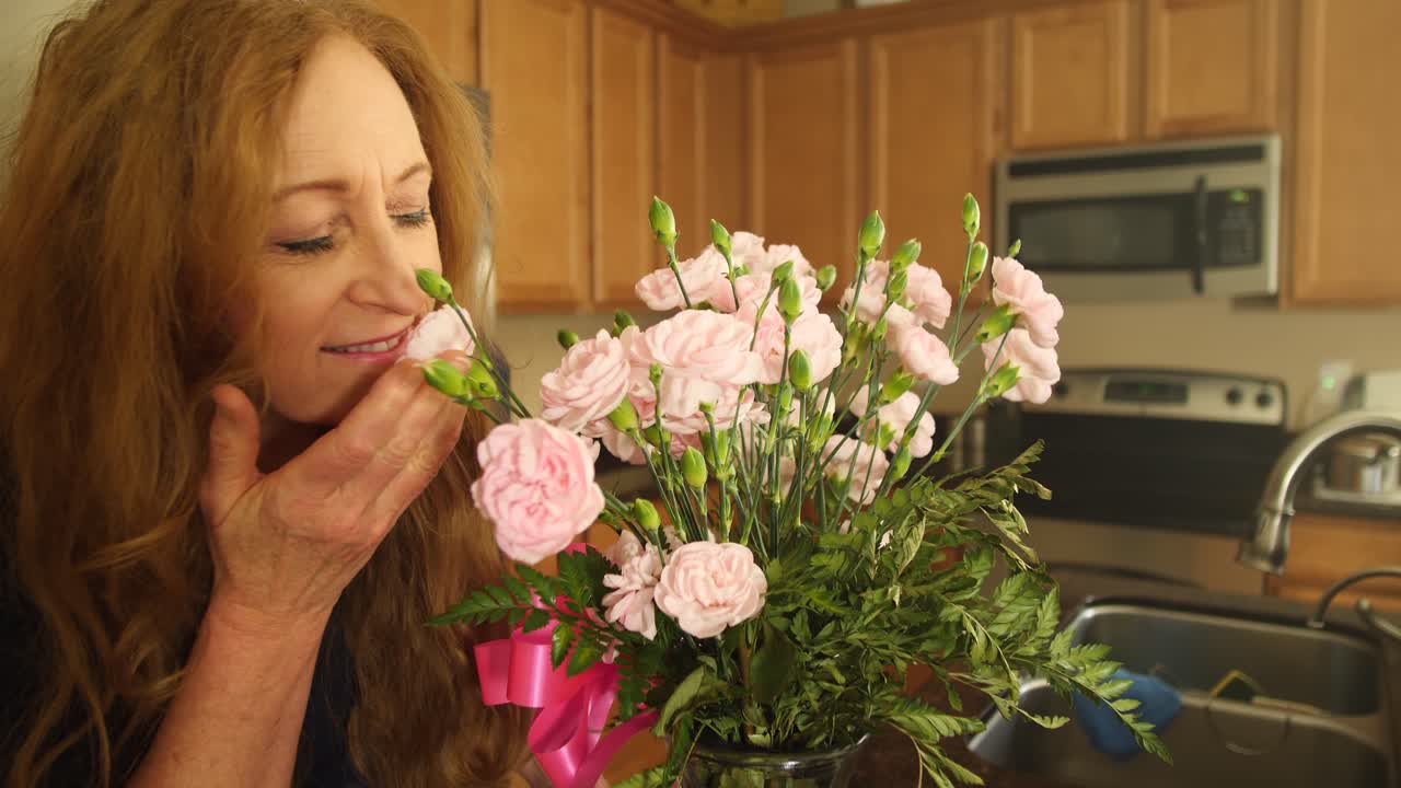 mujer pelirroja huele flores de cerca en una mañana brillante en su cocina