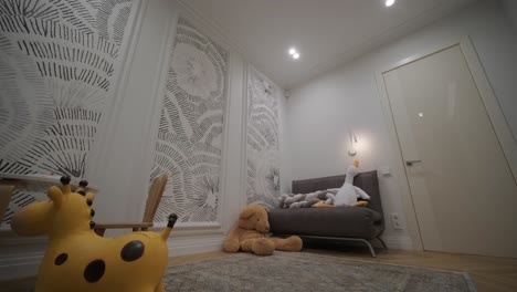 a cozy children's room corner with a playful giraffe toy and a cuddly teddy bear beside a small gray sofa, against a whimsical patterned wallpaper, creates a charming and nurturing space