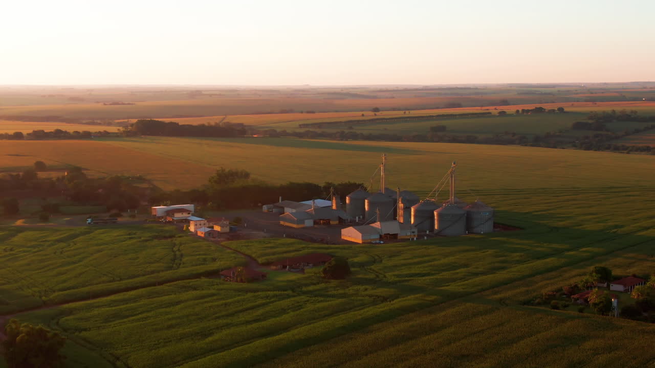 Drone aerial landscape of wheat grain silo tanks at facility factory surrounded by meadow field plantations in outdoor countryside farmland valley in Brazil South America industry agriculture crops.