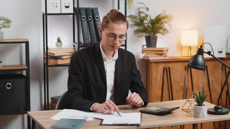 successful businessman analyzing financial report while using calculator sitting at home office desk