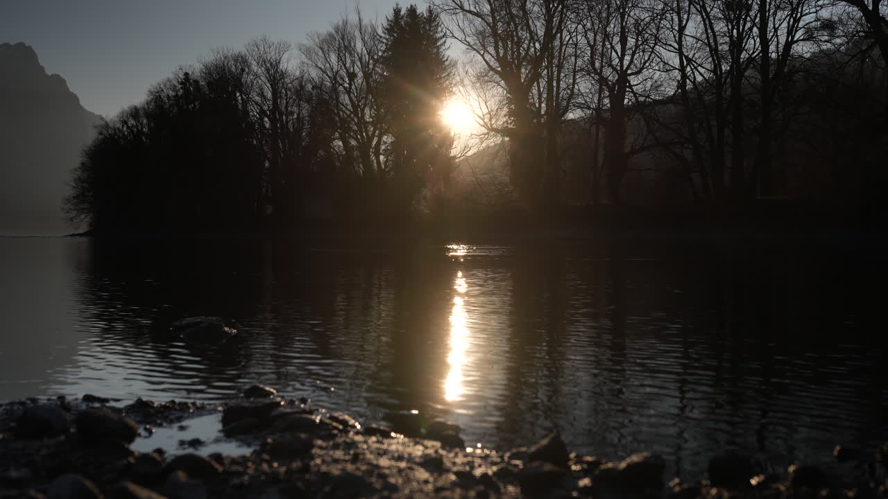Sunlight reflects on quiet lake by trees near Walensee Switzerland