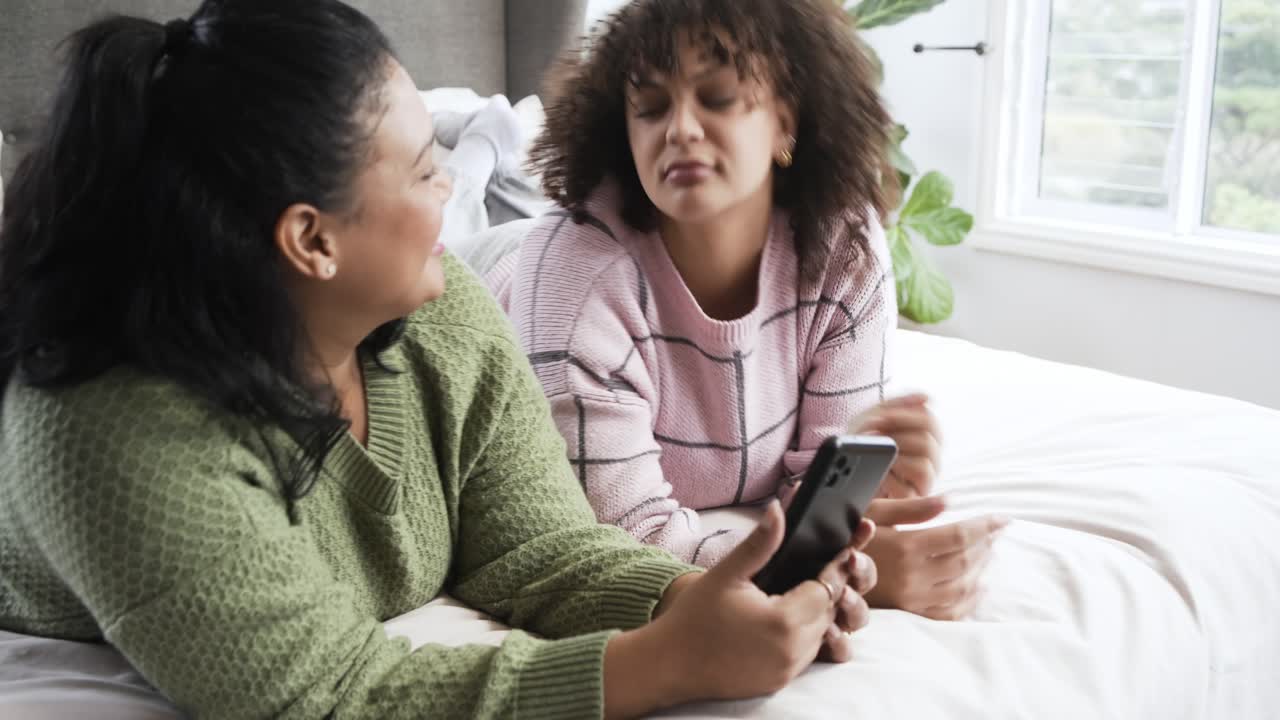 Happy Friends Lying on Bed and Discussing Content on a Smartphone