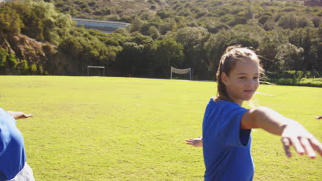 playing on school field, girl in blue shirt stretching arms, smiling outdoors