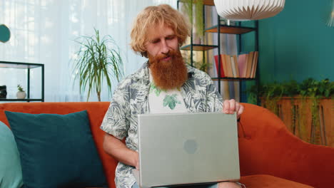 young man freelancer sitting on couch closing laptop pc after finishing work in living room at home