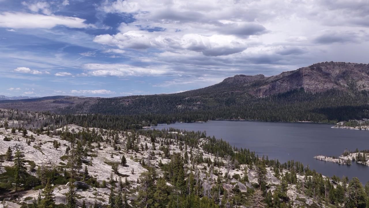 Riprese con drone che catturano la bellezza aspra del Lago Silver a Pioneer, California, mostrando la riva rocciosa, la fitta pineta e il vasto paesaggio montano sotto un cielo parzialmente nuvoloso.