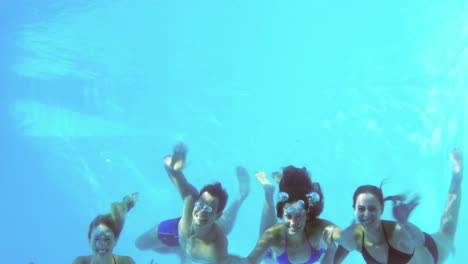 four friends jumping into swimming pool and waving