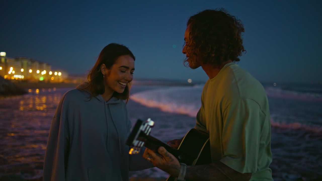 밤 에 기타 를 연주 하는 동안 해변 에서 키스 하는 부부