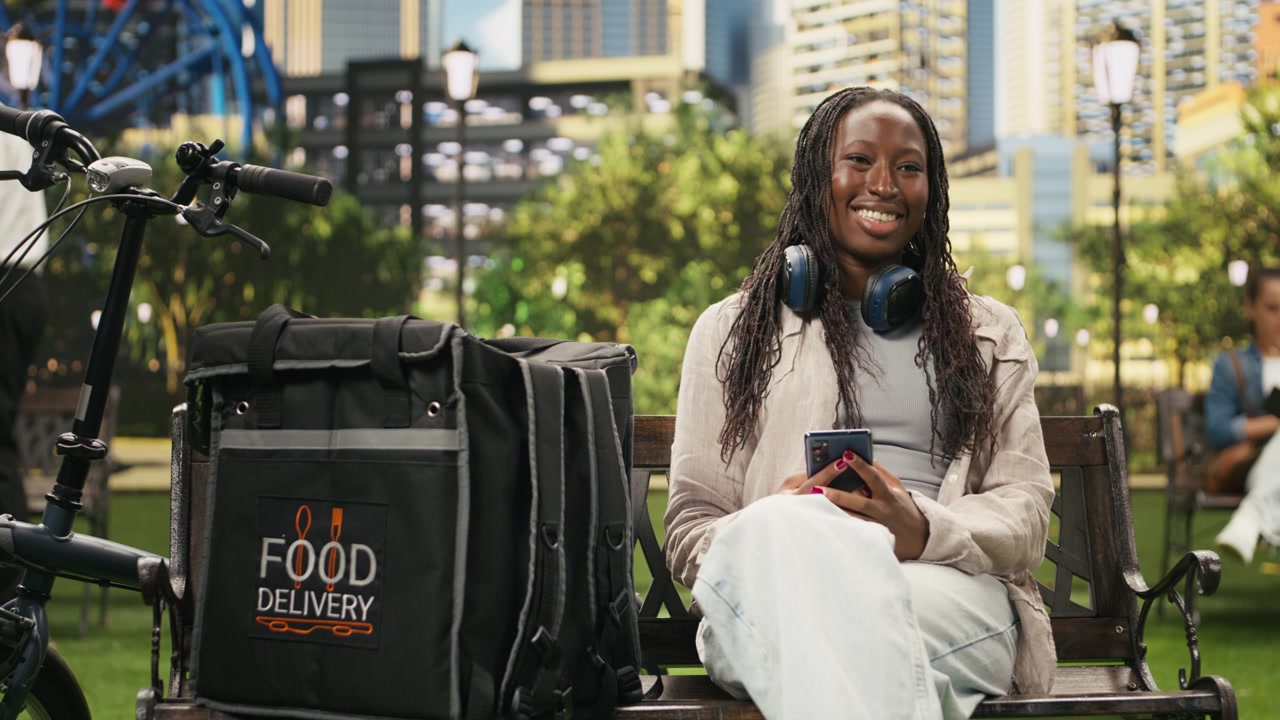 Portrait of smiling courier looking at the camera seated with smartphone