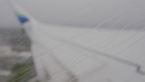 Passenger-POV,-rainy-plane-window-rack-focus-to-wing-during-takeoff,-Seattle