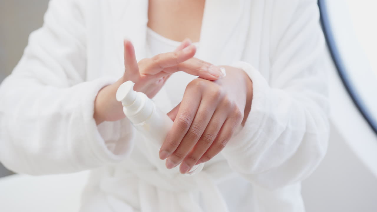 Applying lotion, asian woman in white robe moisturizing hands in spa setting, at home