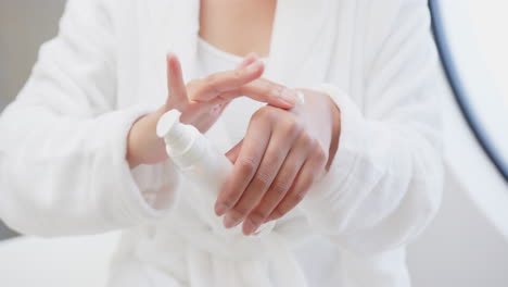 applying lotion, asian woman in white robe moisturizing hands in spa setting, at home