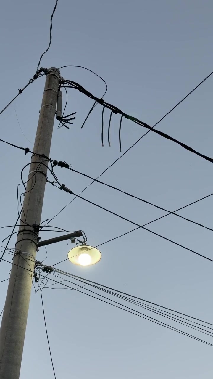 Glowing Street Lamp on Utility Pole Against Evening Sky
