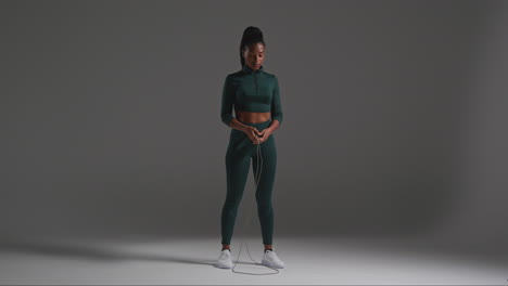 studio full length shot of female athlete wearing tracksuit training in gym fitness class with jump rope or skipping rope against plain background