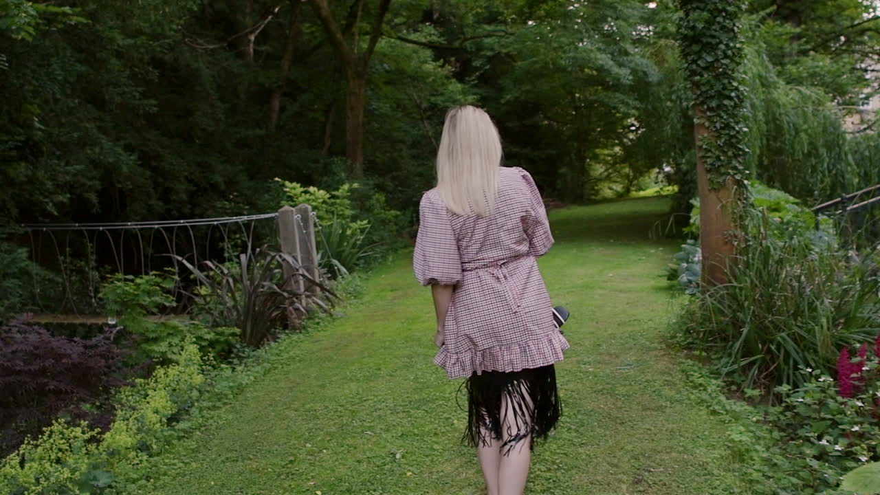 Lovely Woman Fashion Model In Barefoot Looks Back At The Camera As She Walks Through Lush Green Lawn At The Park - Slow Motion