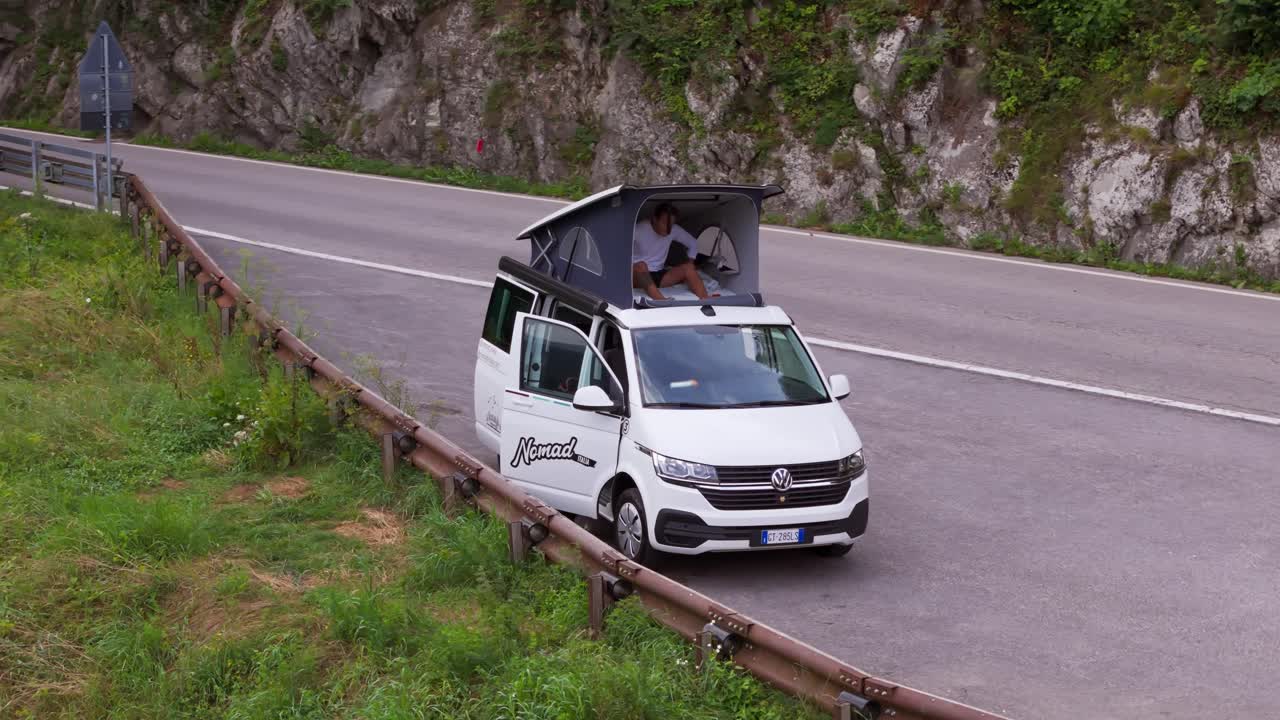 Drone orbits left as solo traveler wakes up on top of camper van in Italian Alps