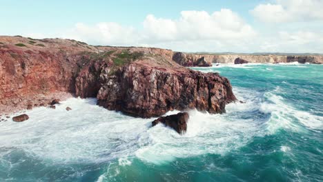 Aerial-4k-drone-push-in-view-of-large-crashing-waves-at-Praia-da-Zimbreirinha-hidden-cliff-coastline-near-Bordeira-in-the-Algarve-region-of-Portugal