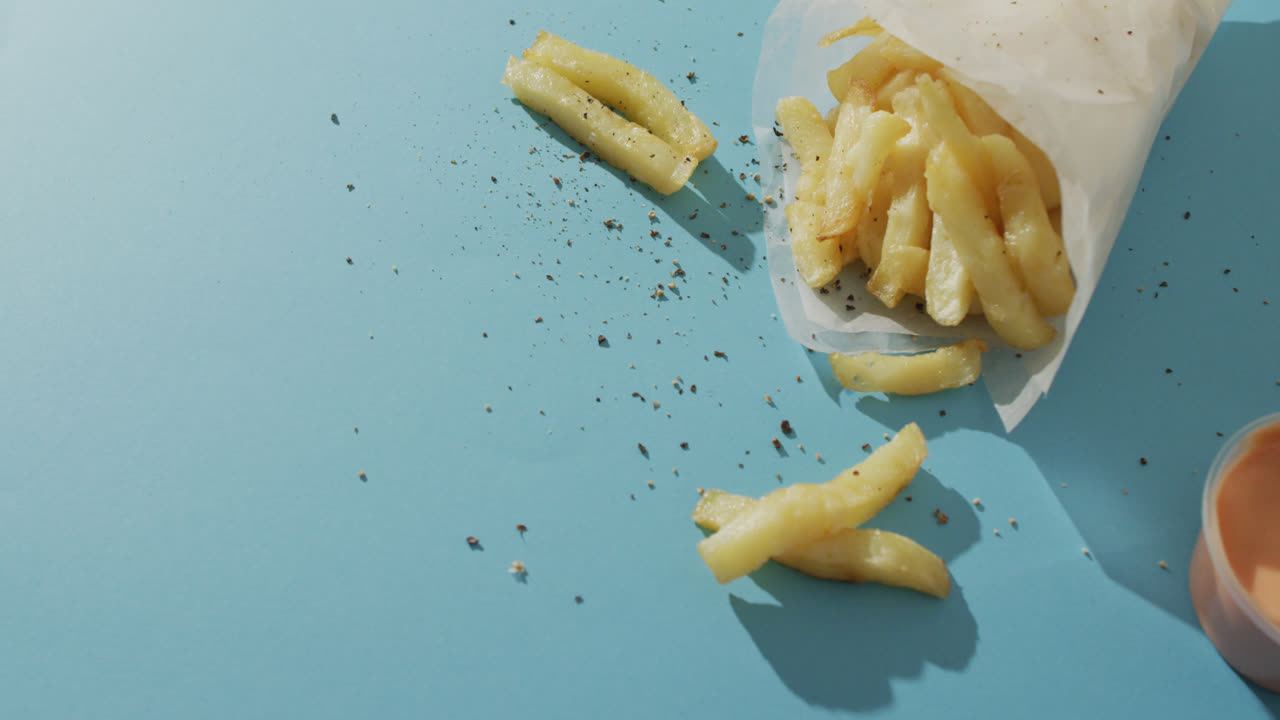 Video of chips wrapped in paper, salt and pepper and dip, with copy space on blue background