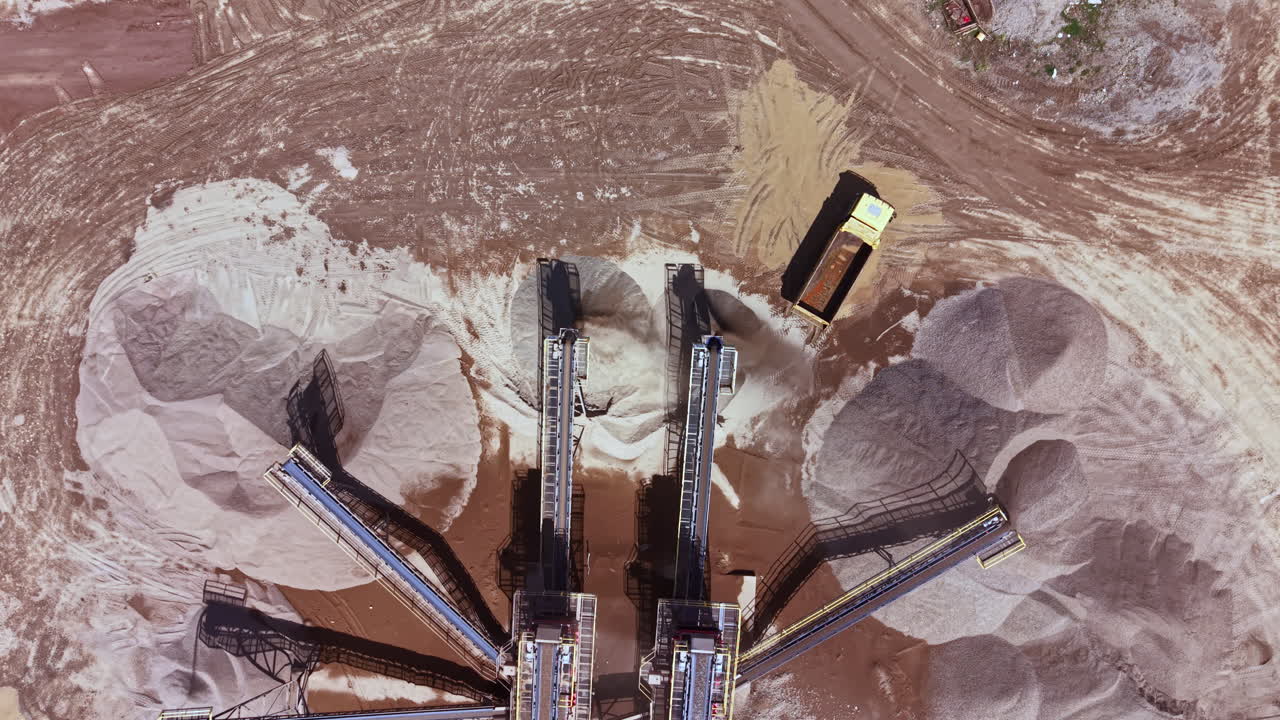 Activity at a sand and gravel processing site shows machinery moving materials in a construction area during daytime hours