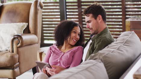 Smiling-mixed-race-couple-using-digital-tablet-together-on-the-couch-at-vacation-home