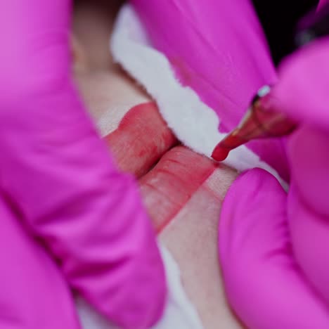 tattoo machine doing makeup on woman's lips. hands in pink gloves of a professional cosmetologist making permanent makeup on lips. close-up.