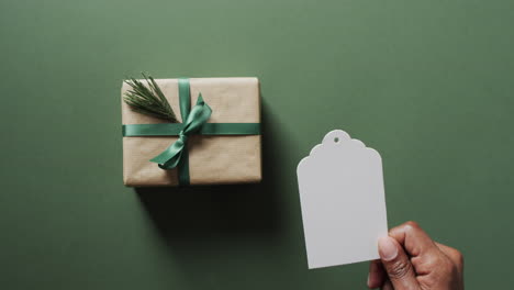 Video-of-christmas-presents-and-hand-holding-white-tag-with-copy-space-on-green-background