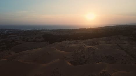 Golden-hour-aerial-over-red-sand-dune-landscape-of-Mui-Ne,-Vietnam