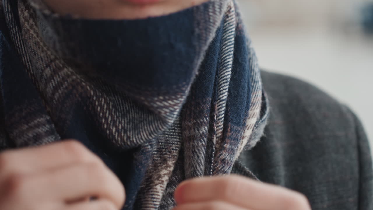 Creatore che sistema sciarpa e orologio, primo piano delle mani, sciarpa di lana, cappotto scuro, strada invernale dai colori tenui, movimenti lenti e deliberati, texture tattili, rivelazione di un orologio di lusso, messa a fuoco cinematografica ridotta.
