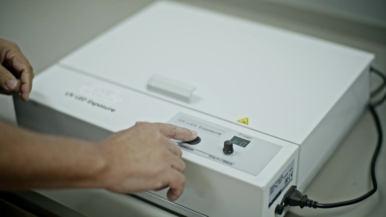 lose up shot of a technician's hands pressing buttons on the control panel of a white UV LED exposure machine in a laboratory