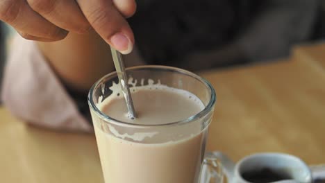 woman stirring coffee in a glass cup