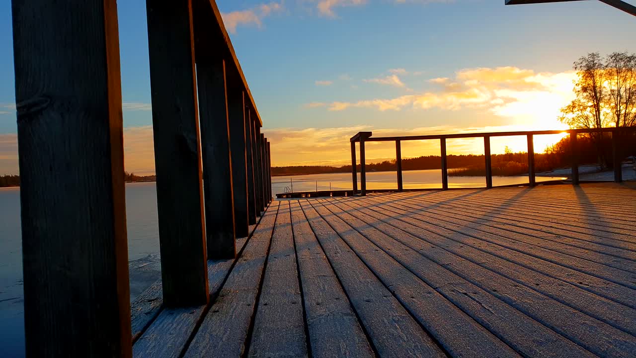magical winter sky with golden clouds in Finland, static shot from a public wood deck in early December, sun casting long shadows
