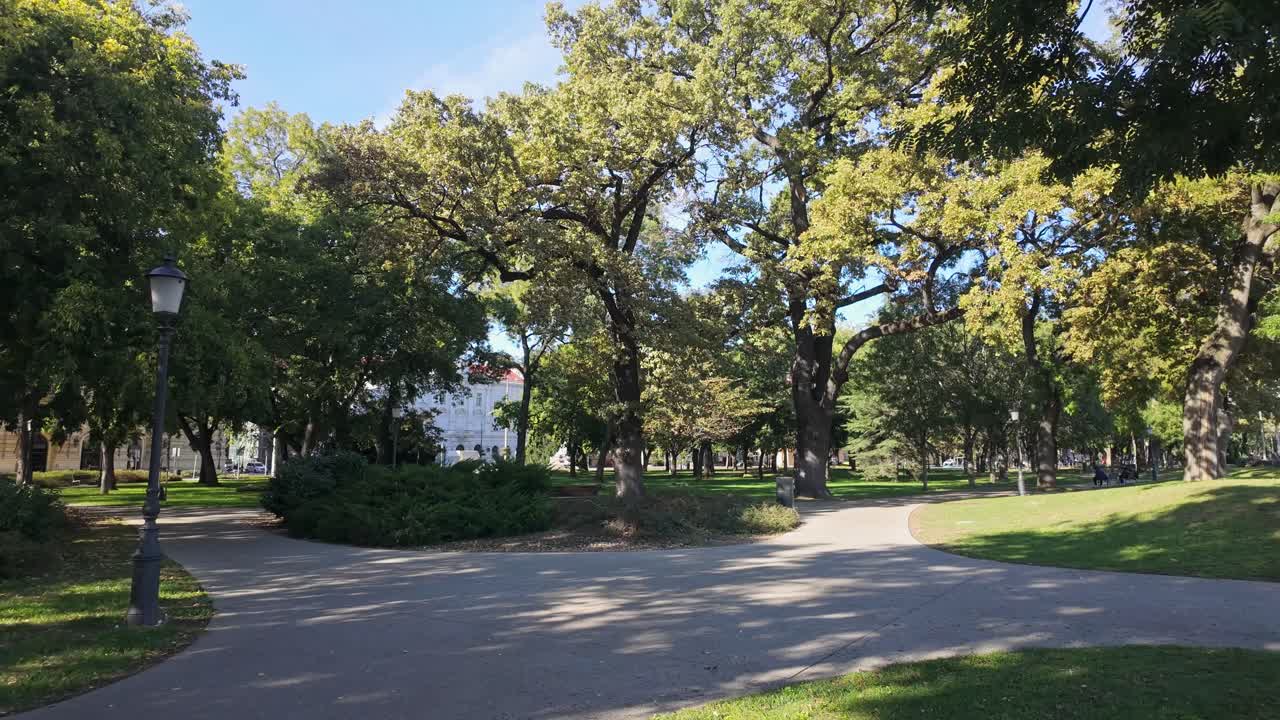 The Varkert park in Szeged city center, Hungary, featuring lush trees, pathways, and a relaxing sunny atmosphere