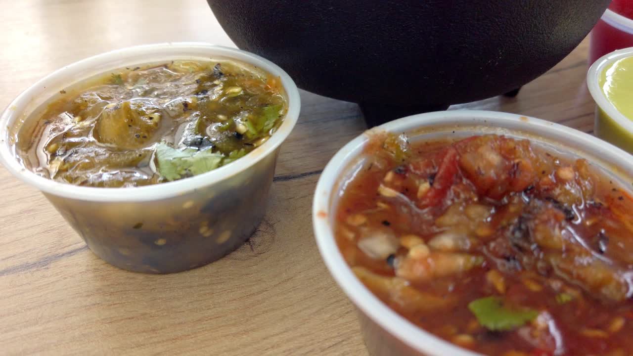 Close up of traditional Mexican green salsa in plastic container on wooden table with visible seeds and cilantro