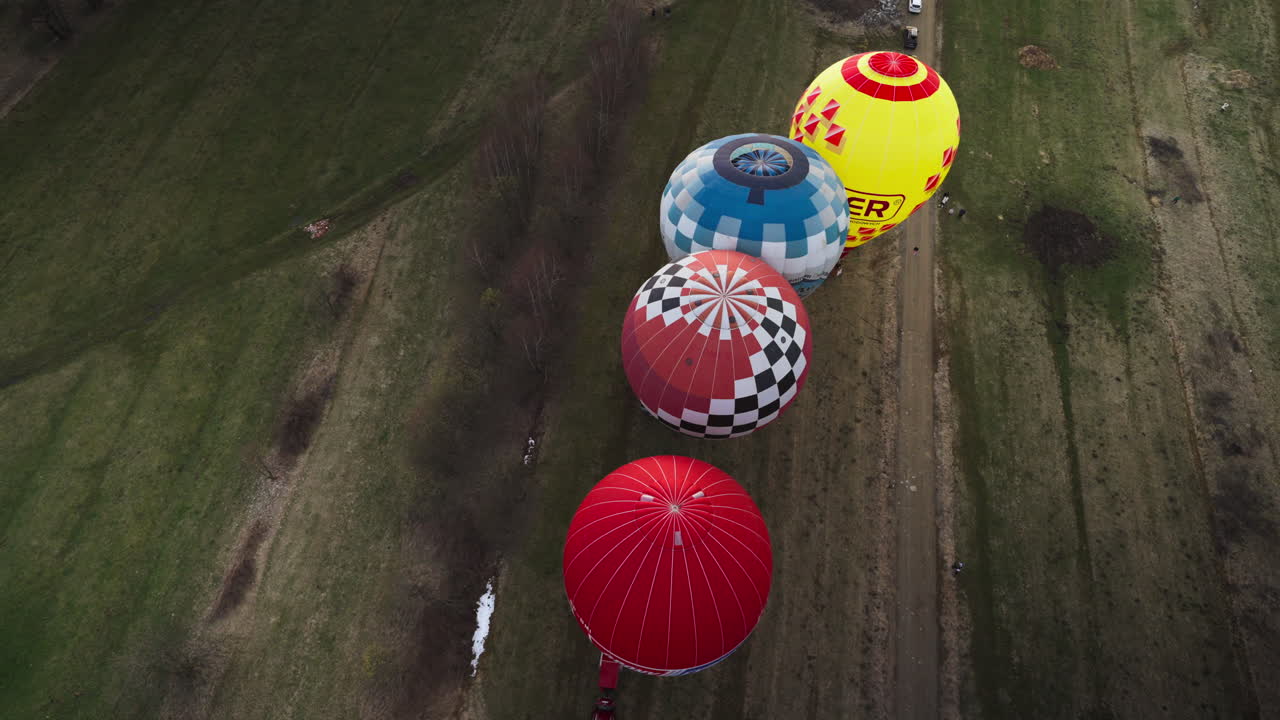 Handheld shot of four hot-air balloons landing on the ground in the day