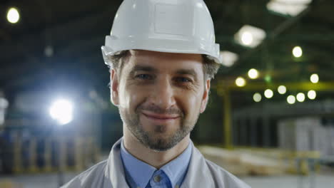 vista de cerca del ingeniero caucásico con casco y girando la cabeza hacia la cámara y sonriendo en una fábrica