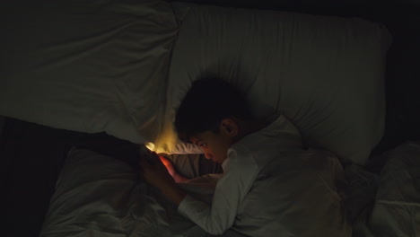 Young-Boy-In-Bedroom-At-Home-Lying-In-Bed-Using-Mobile-Phone-To-Text-Message-At-Night-1