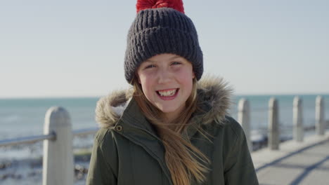 portrait of happy little girl on beach smiling cheerful dressed warm wearing beanie hat and coat