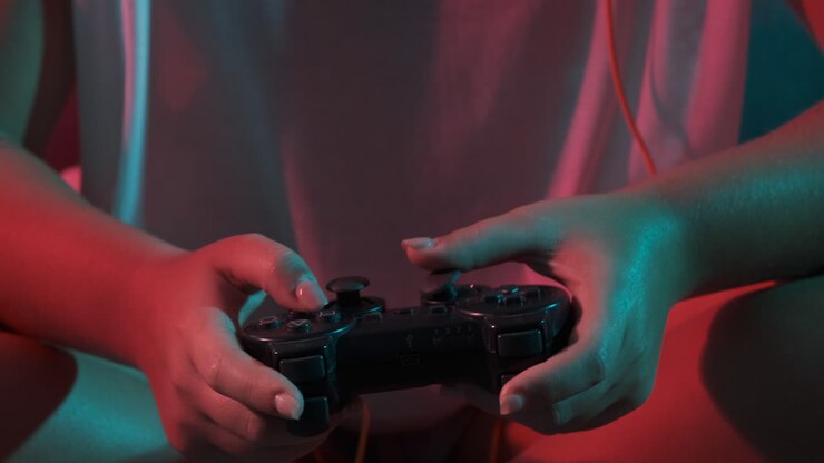Primo piano delle mani di una donna con un controller per console di gioco mentre gioca. Luci colorate.