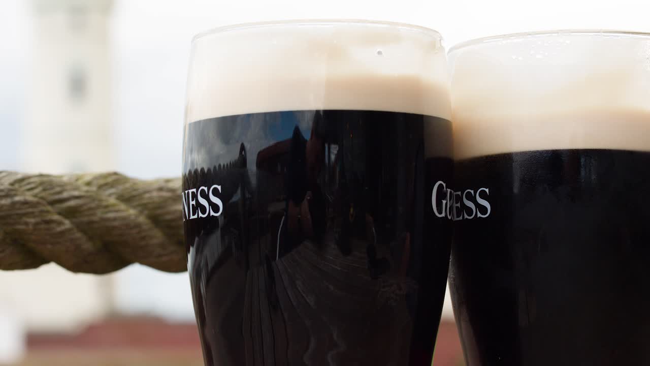 Two pints of dark beer clink together outdoors, natural daylight, shallow focus, relaxed mood