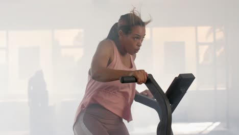 determined unaltered biracial woman training on elliptical bike at gym, in slow motion