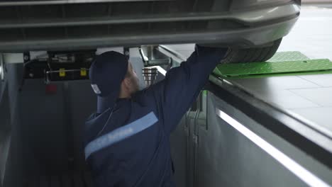 mecánico en uniforme reparando la parte inferior de un coche usando herramientas.