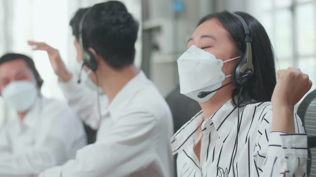 Close Up Of Three Asian Call Center Agents Wearing Headsets And Masks Being Happy Due To Success Working At The Office