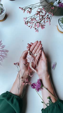 rose quartz crystal charm in hands, surrounded by flowers