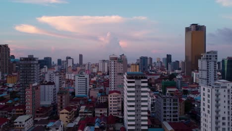 drone view over phnom penh city skyline in the evening, aerial drone shot, trucking left, roof level, with distant thunderstorm cloud in the distance and bright vivid colours of the buildings