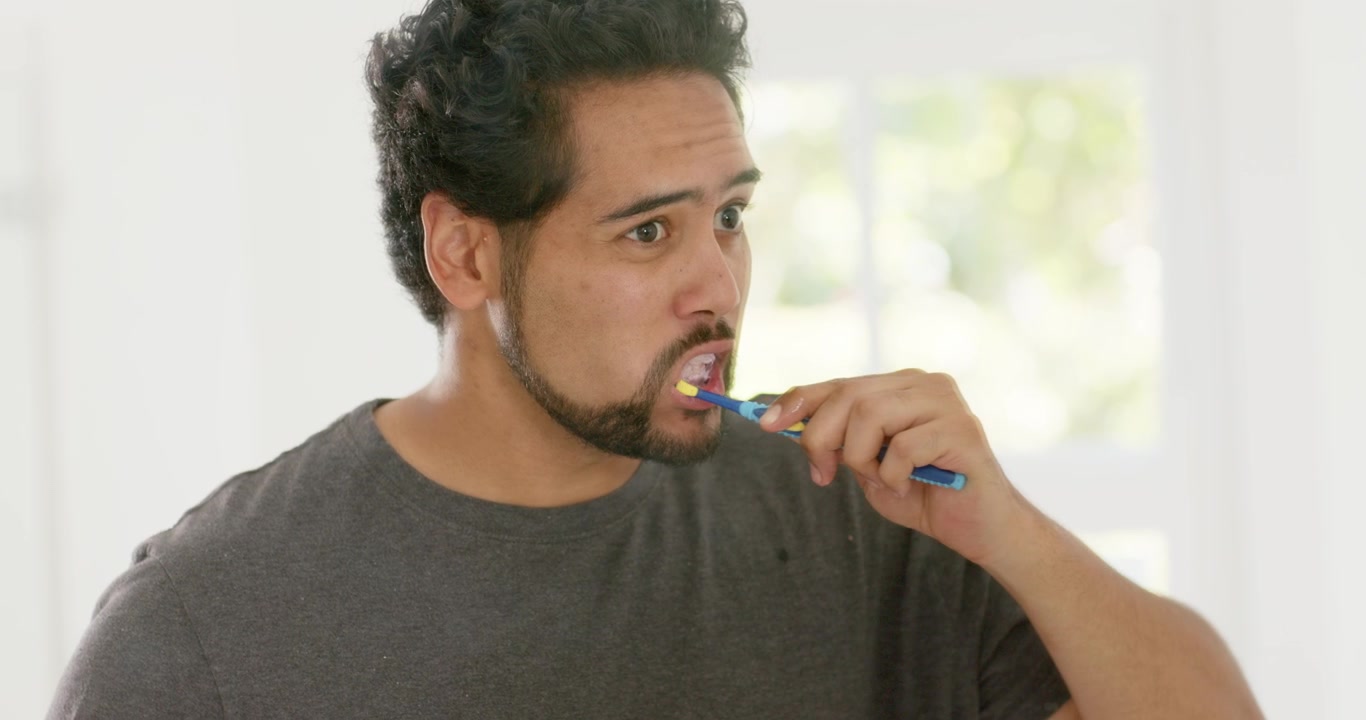 Mid-adult African American man raising blue toothbrush, brushing teeth, checking mirror for hygiene