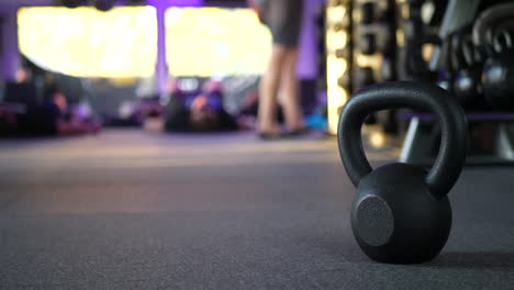 Un-Peso-De-Pesas-Rusas-En-Un-Gimnasio-Con-Gente-Haciendo-Ejercicio-En-Una-Clase-De-Entrenamiento-Físico-En-El-Fondo