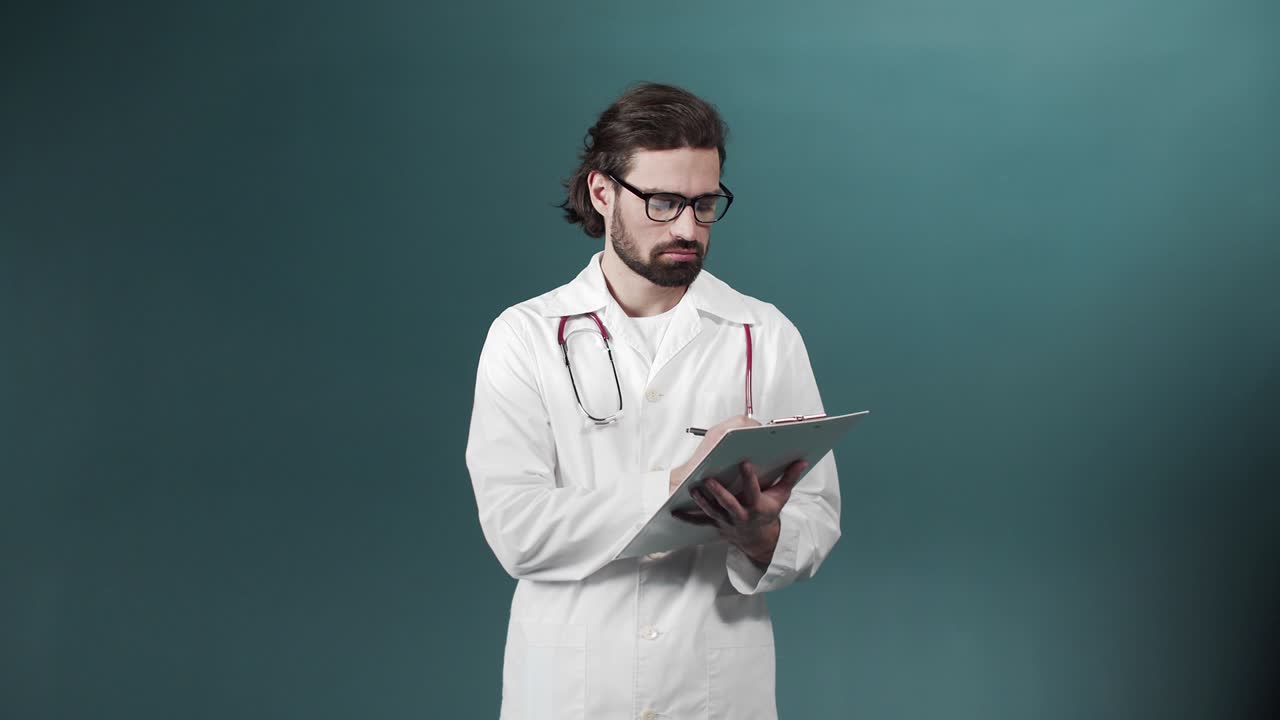 Un giovane medico in camice bianco sta scrivendo qualcosa su un tablet che tiene in mano.