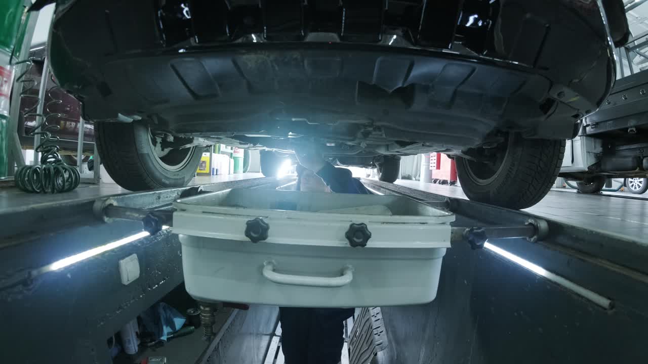 피트에 있는 기계공이 차 바닥을 확인합니다.