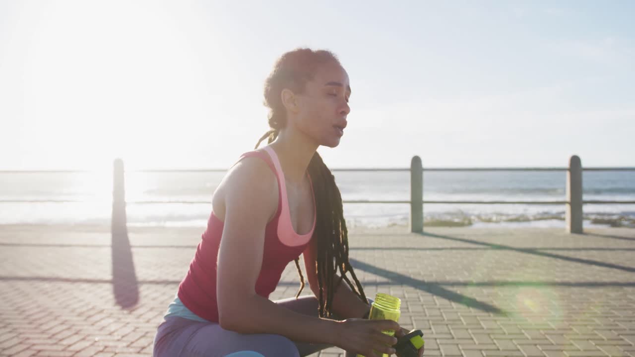 mujer afroamericana haciendo ejercicio bebiendo agua en el paseo marítimo