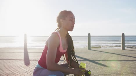 african american woman exericisng drinking water on promenade by the sea